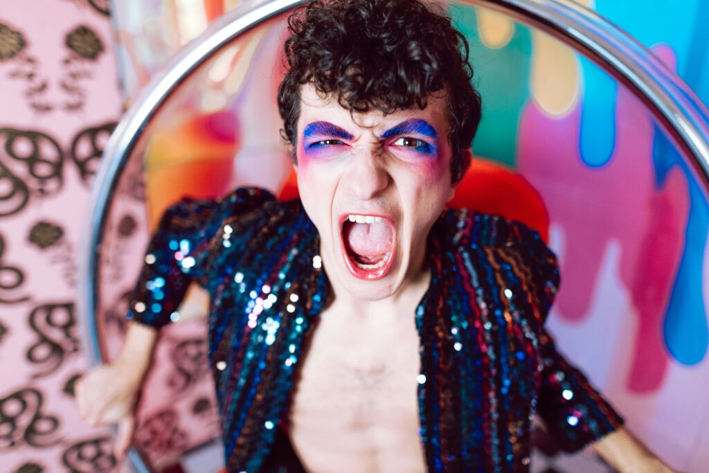 Energetic portrait of a young adult with colorful makeup and a vibrant sequin outfit, showcasing bold expression.